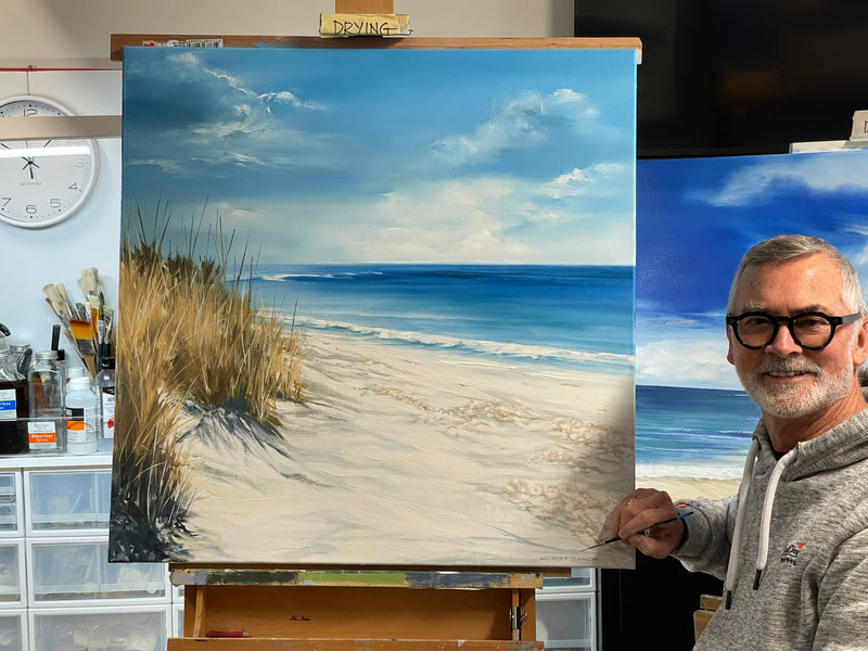Geoff Barlow beside a coastal painting on his studio easel