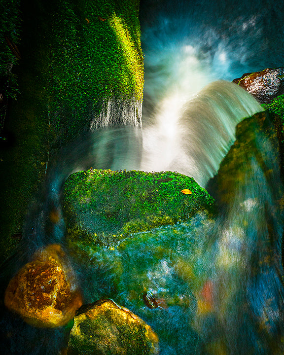 Photograph of mossy rocks and a waterfall in a natural setting