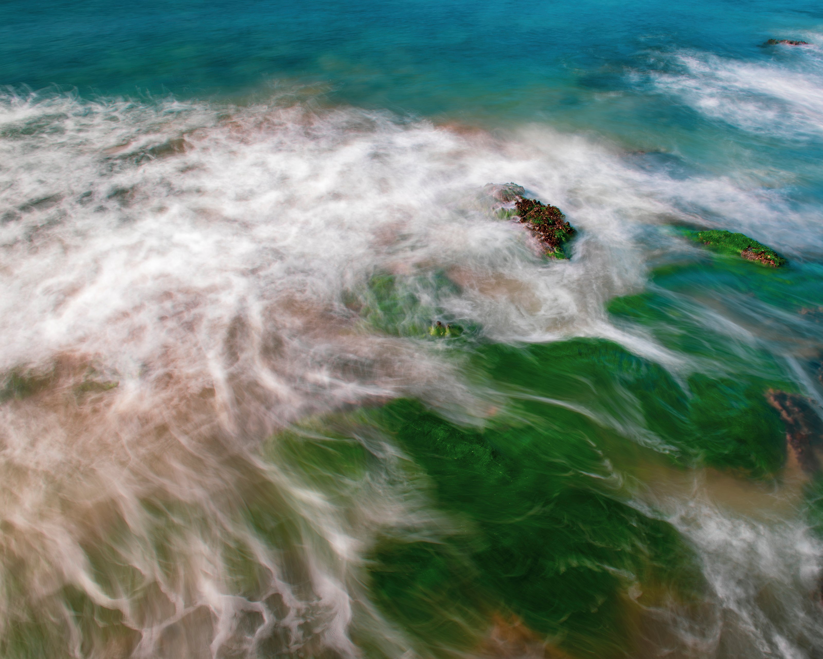 Abstract photo of ocean waves with, rocks, white foam, green seaweed and turquoise water