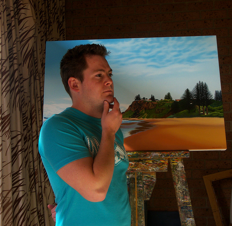 Mark Kingston beside a coastal painting in his studio