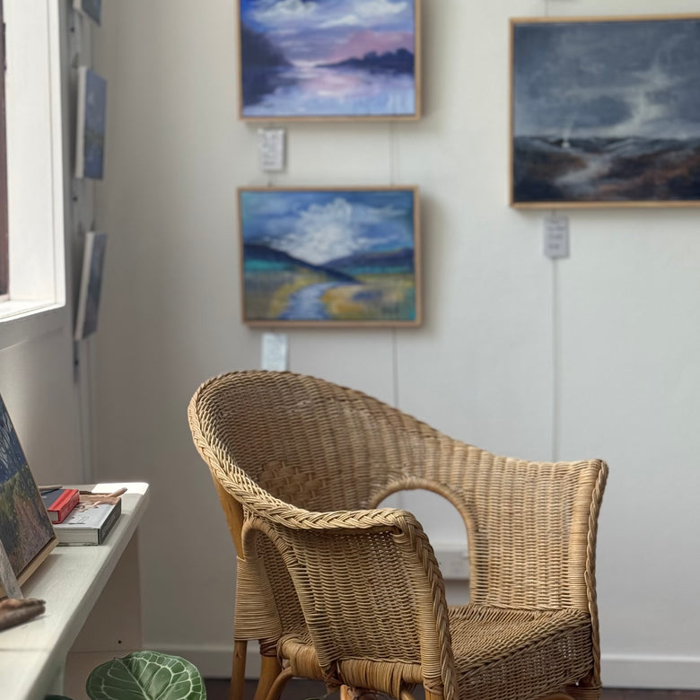 Wicker chair in front of wall with framed landscape paintings