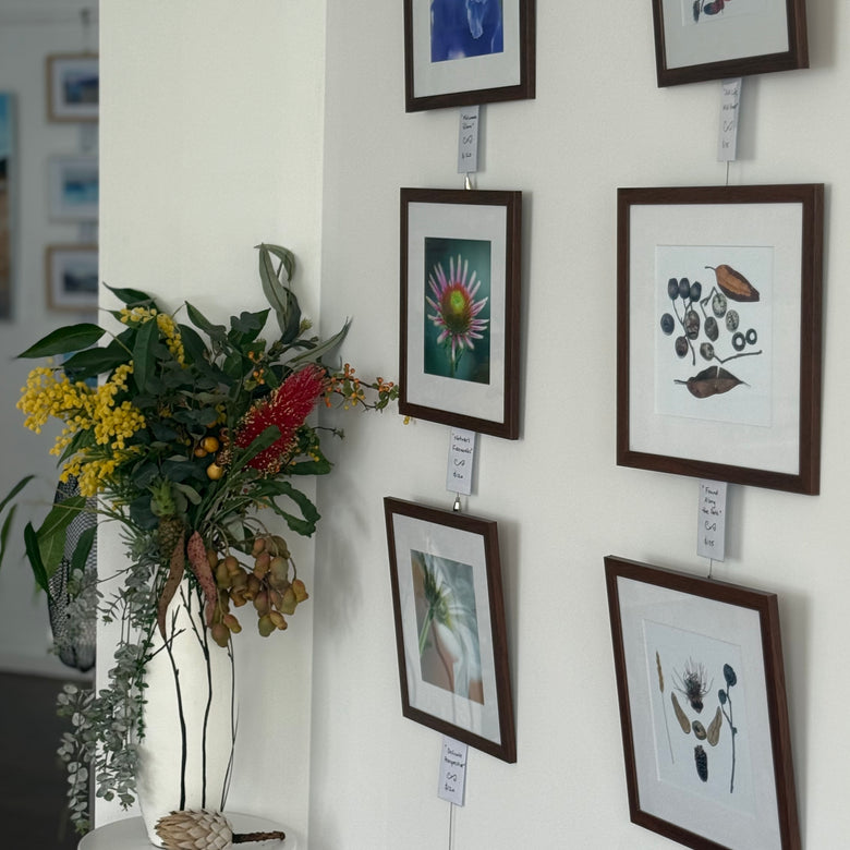 Artistic wall display with framed artworks and a vase of flowers on a white pedestal.